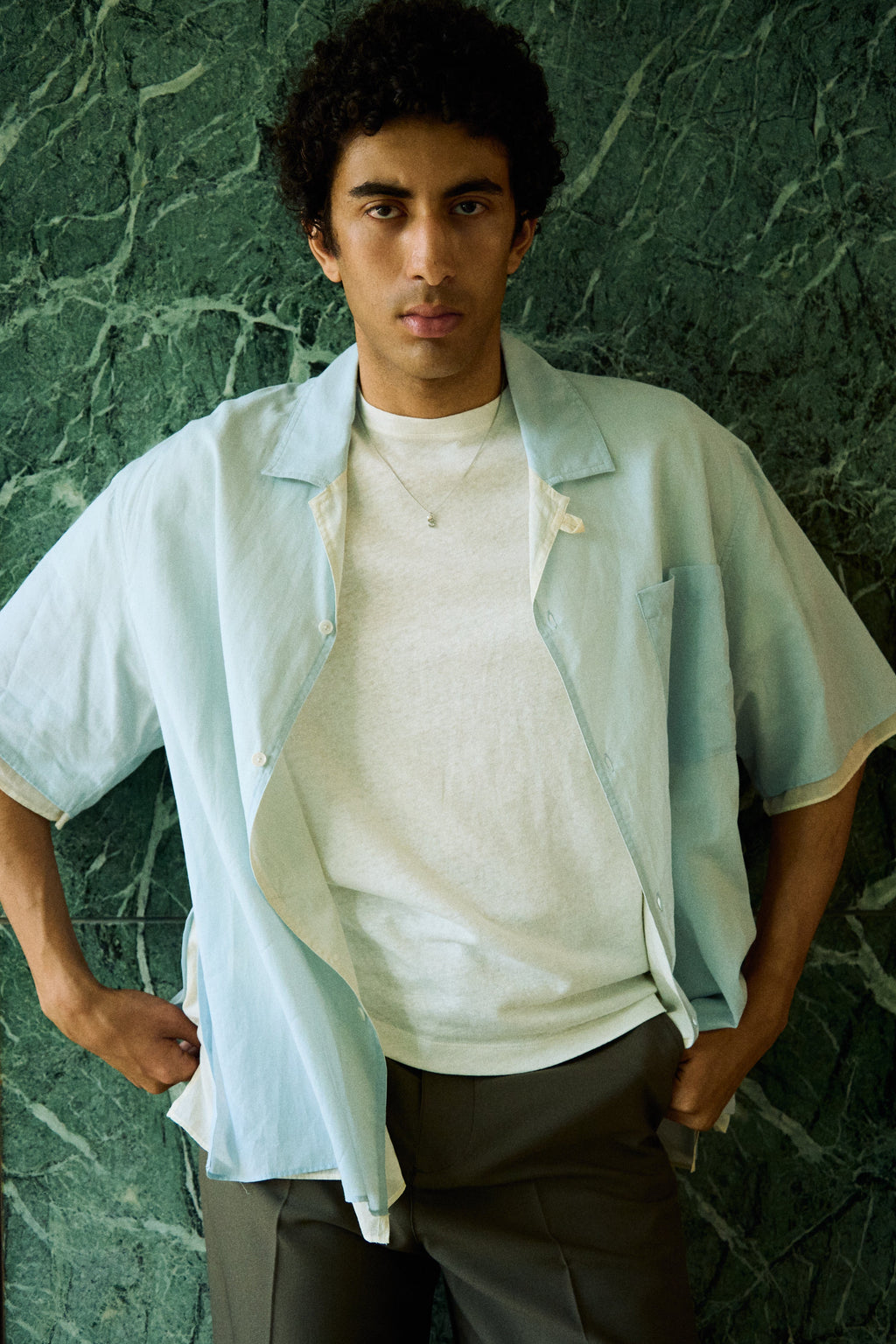 Man wearing a minimal initial necklace with a small letter pendant on a longer chain.
