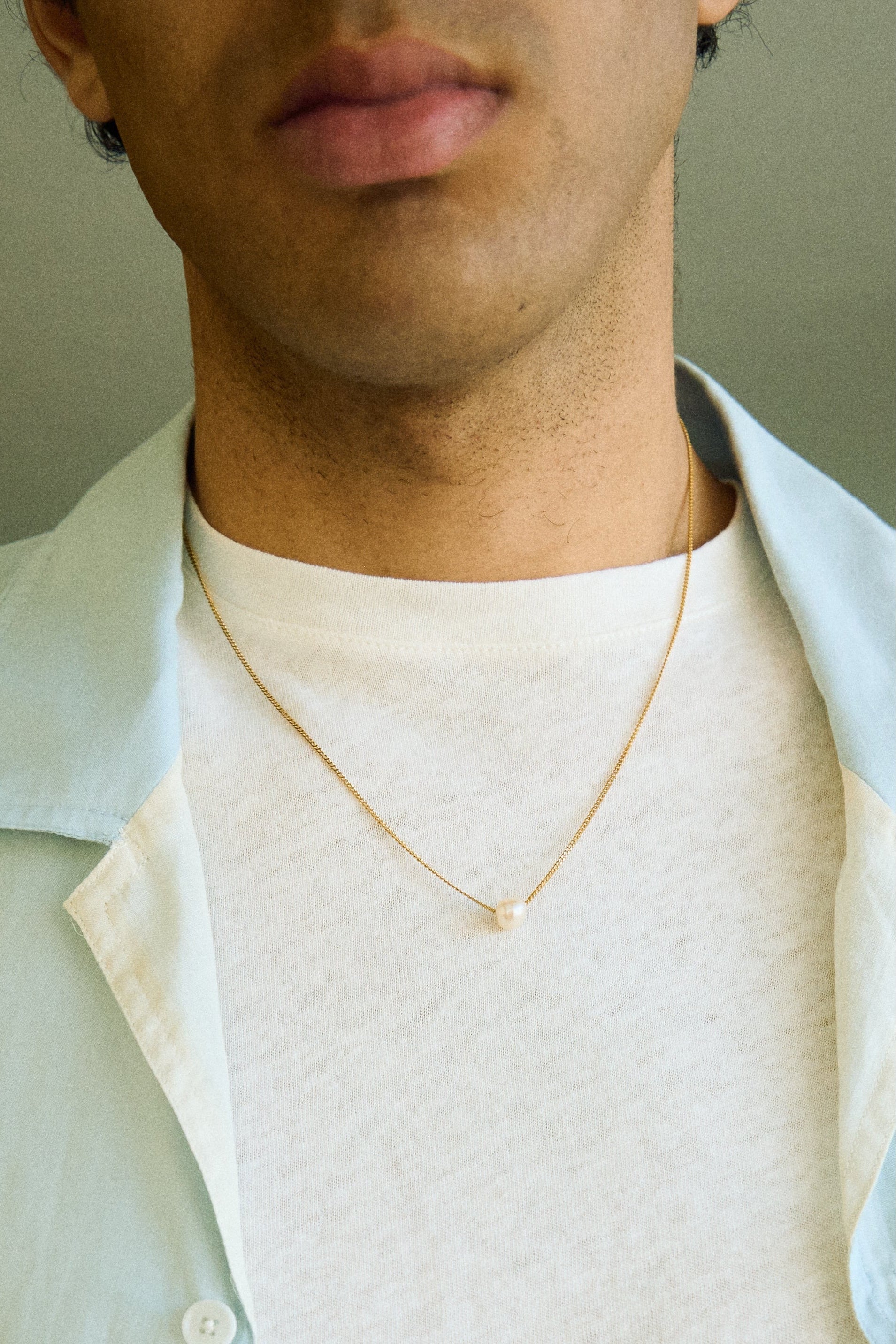 Man wearing a minimal single pearl necklace on a fine chain.