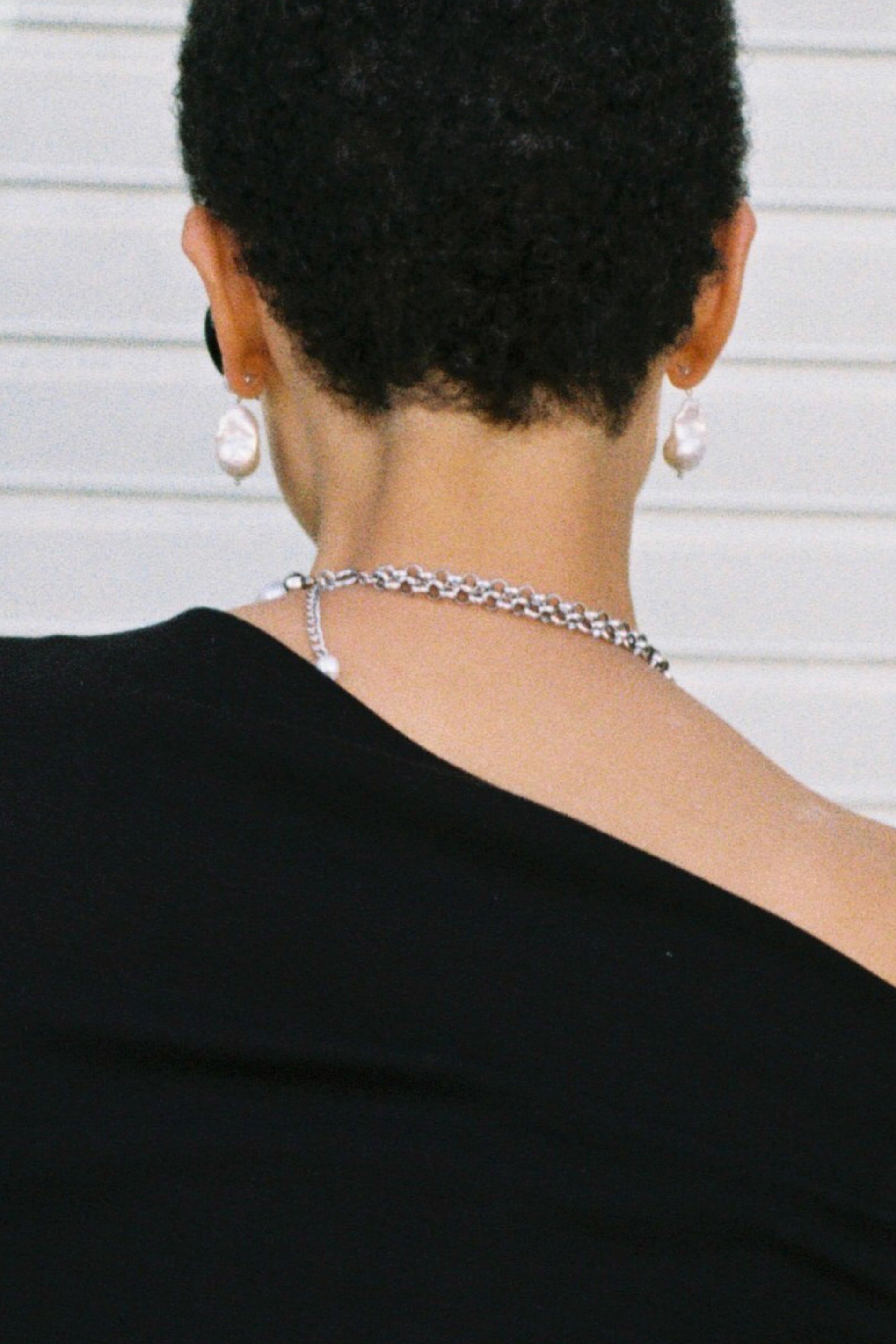Person wearing a silver chain necklace with a plain background