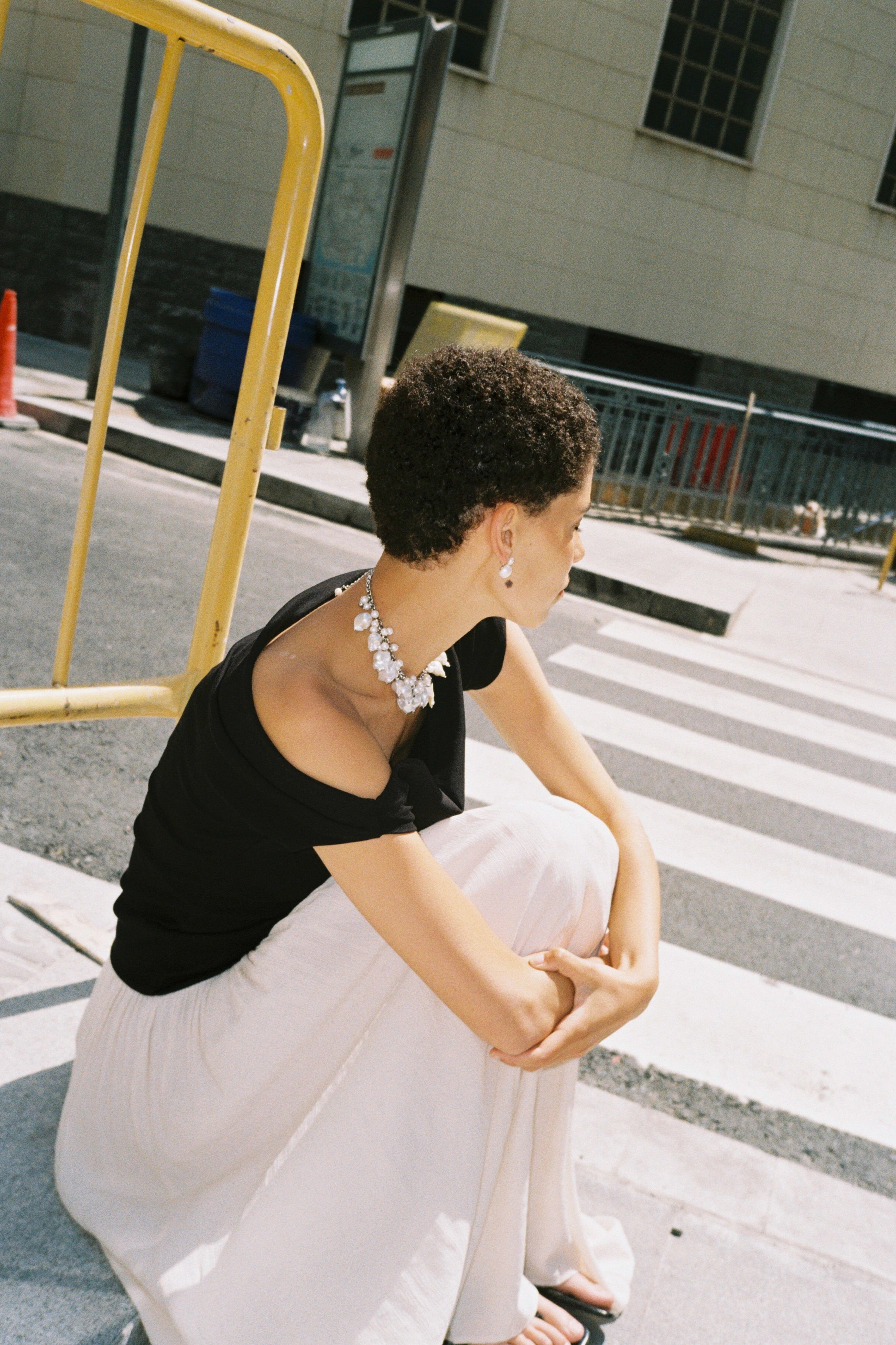 Woman sitting on a step wearing a black top and white pants with a necklace.