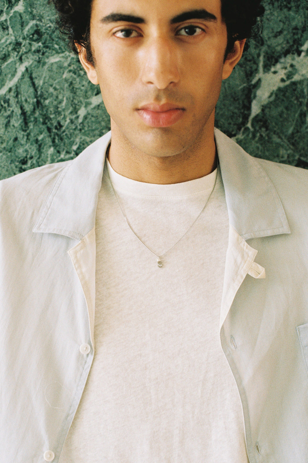 Man wearing a minimal initial necklace with a small letter pendant on a longer chain.